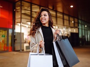 Mujer joven con bolsas de la compra cerca de centro comercial. Estilo primaveral. Consumismo, compras, estilo de vida, concepto de venta.
